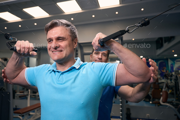 Contented man performing strength exercise with personal trainer