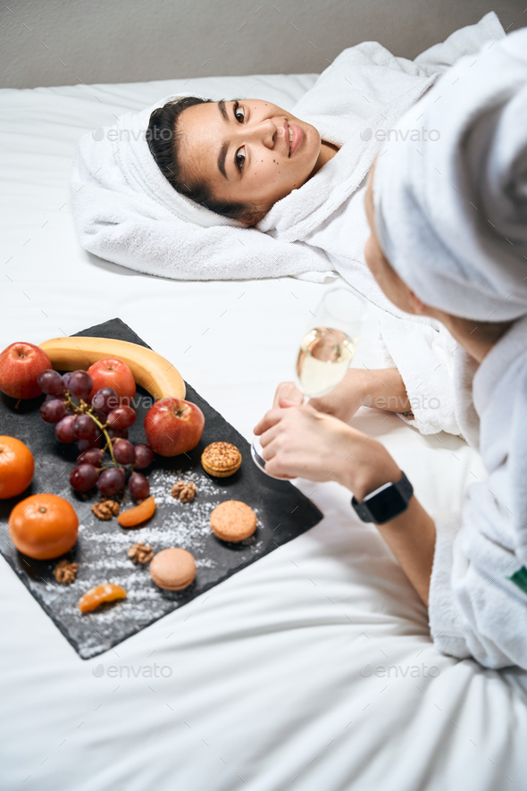 Cropped photo female on hotel bed in bathrobes and fruits