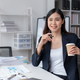 Successful Asian businesswoman smiling using laptop computer and holding coffee cup at office.  - PhotoDune Item for Sale