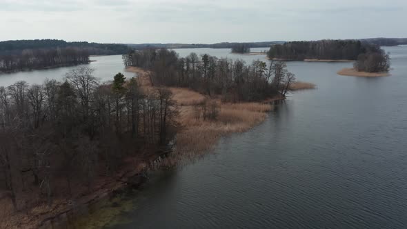 AERIAL: Small Island in the Lake with Reeds and Trees on them on a Gloomy Dull Spring Windy Day