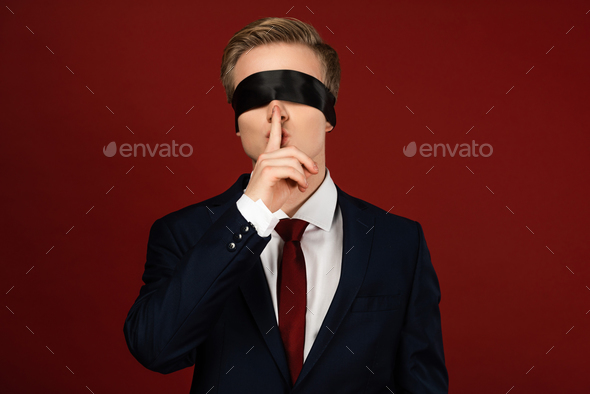 man with blindfold on eyes showing shh gesture on red background