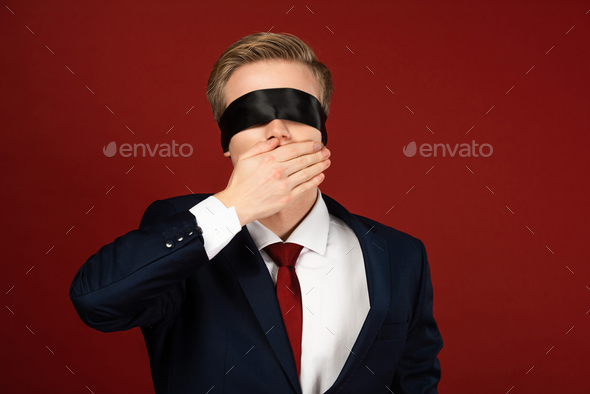 man with blindfold on eyes covering mouth with hand on red background