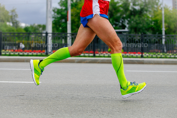 close-up legs runner athlete running marathon in city in green compression socks, sports summer race