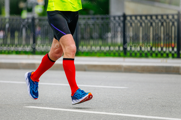 male runner athlete running marathon in city in red compression socks on feet, sports summer race