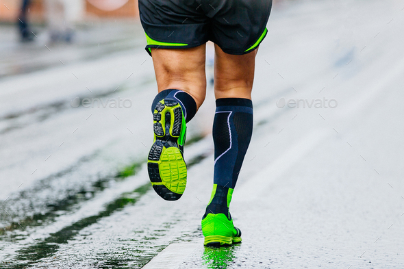 close-up legs runner athlete running marathon in black compression socks, male run on wet asphalt