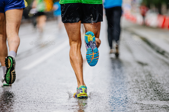 legs male runner athlete run marathon race on wet asphalt, water drops on sole running shoes