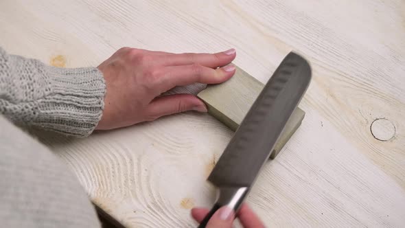Close-up of a woman sharpening a kitchen knife on a table alt