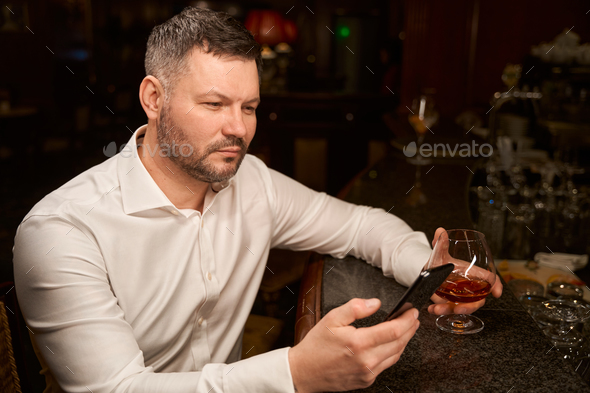 Handsome man with smartphone sitting alone at bar counter