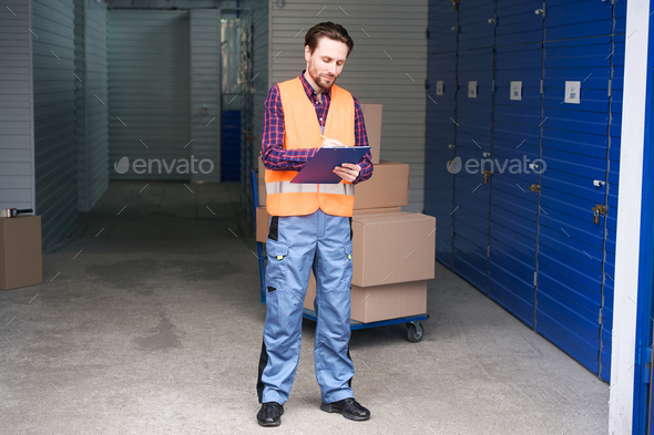 Full length of young man in work clothes into warehouse with self storage unit