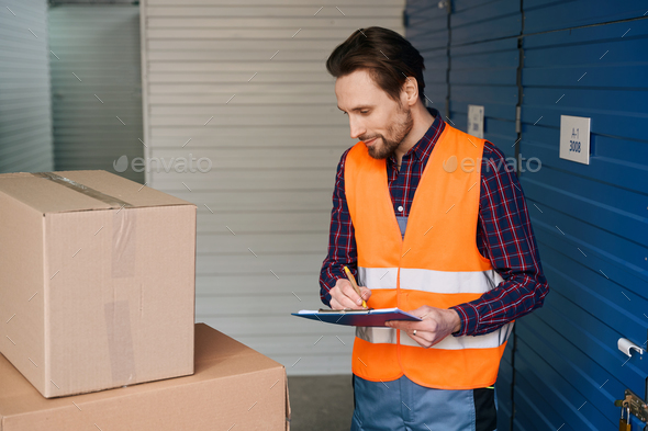Waist-up of man in work clothes with boxes into warehouse with self storage unit