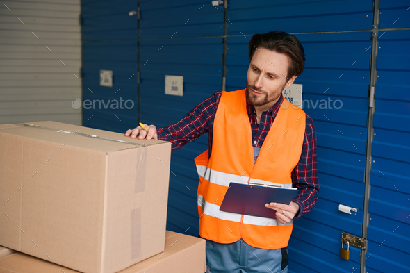 Waist-up of guy in work clothes with boxes into warehouse with self storage unit