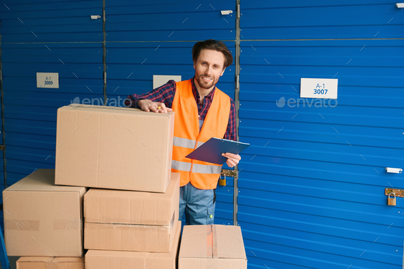 Young man in work clothes with boxes into warehouse with self storage unit