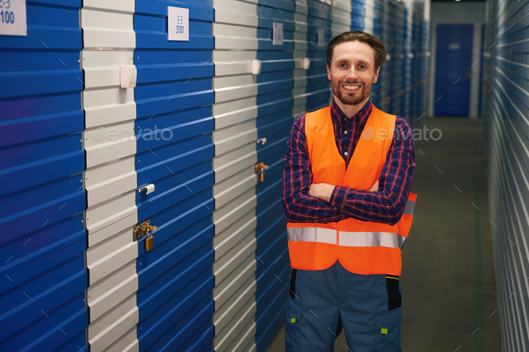 Waist-up of young man in work clothes into warehouse with self-storage unit