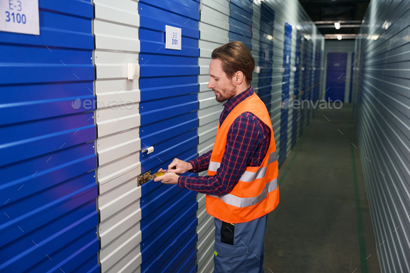 Side view of young guy in work clothes into warehouse with self-storage unit