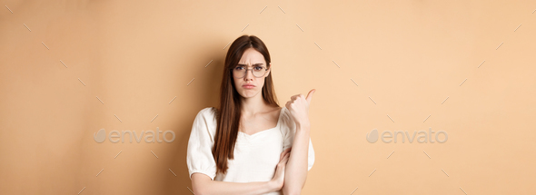 Disappointed girl in glasses frowning, pointing aside at bad product, disapprove and dislike