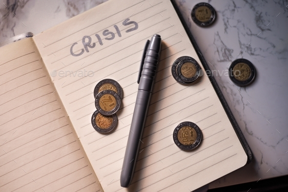Closeup of a block-note with a marker and coins on it and [crisis] written on a sheet on the table
