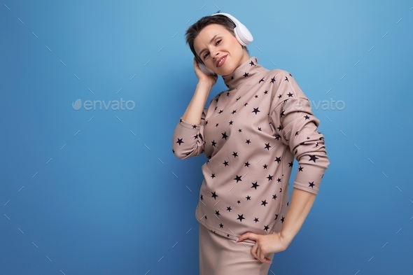 active bright caucasian young woman with a short haircut dressed in a beige suit listens to music in