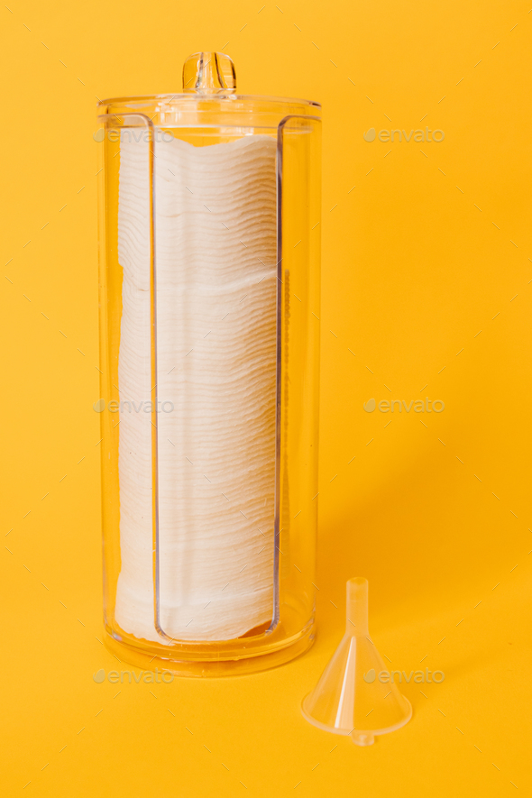 Container organizer for cotton pads and a plastic funnel for spilling liquids on a yellow background