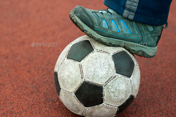 Human foot in a dirty sneaker on an old soccer ball.