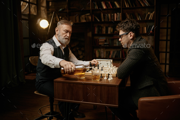 Elderly father and millennial son playing chess and drinking whisky