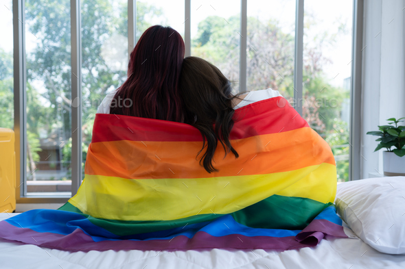 The LGBT couple sat on the bed, covered in rainbow flags, peering out the window