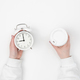 Alarm clock and disposable cup in female hand on white background, top view. - PhotoDune Item for Sale