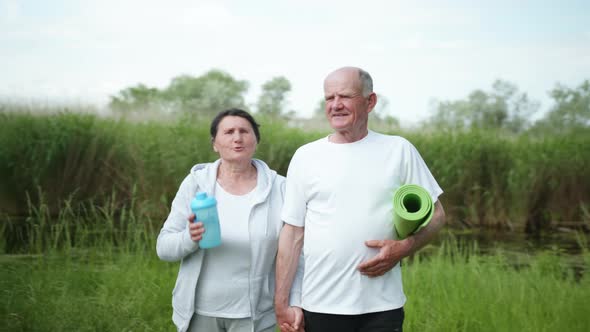 Cheerful Old Man and Woman Take Care of Their Health Go Holding Hands After a Morning Workout alt