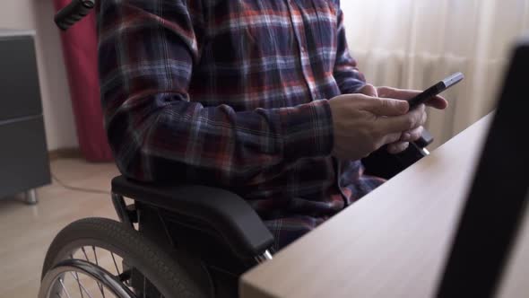 A Disabled Worker Sitting in a Wheelchair Uses a Smartphone