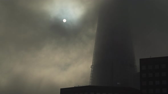 The Shard in London with dramatic moody clouds and mist moving and the sun rising on a misty foggy m alt