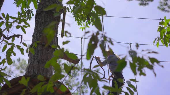 A Young Woman in an Adventure Park. She Wears a Safety Harness. She Climbs on a High Rope Trail alt