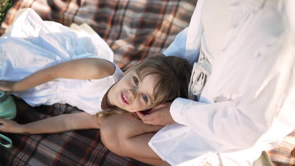 High Angle View of Cute Caucasian Little Girl Looking at Camera Lying on Lap of Unrecognizable Woman alt