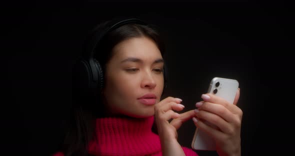 Woman in a Bright Pink Sweater Listens to Music with Headphones Through Phone