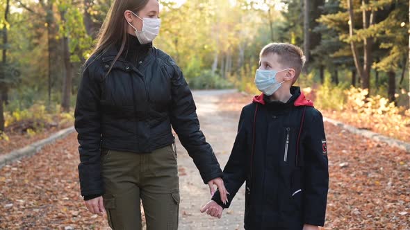 Woman and Her Son at an Empty Autumn Park Wearing Face Masks for Protection Against Virus