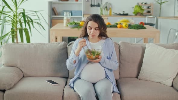 Pregnant Woman With Great Pleasure Eating Vegetable Salad on the Couch alt