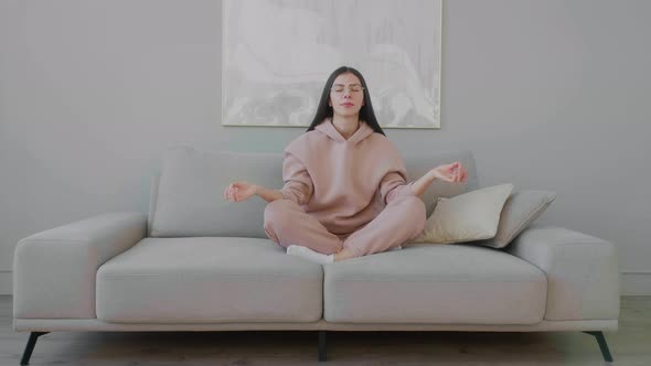 Young Caucasian woman with glasses sitting and meditation on sofa in a lotus position. 