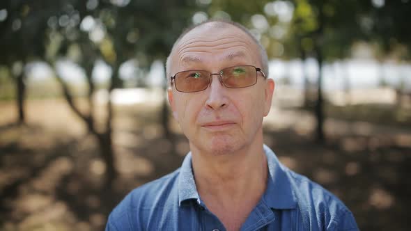 Portrait of Elderly Man with Glasses in the Park Looking at the Camera