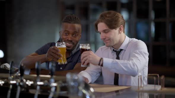 Two Happy Joyful Relaxed Men Clinking Beer Glasses Smiling Toasting Looking at Camera alt