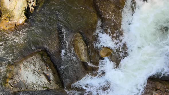 Top down aerial view of small mountain stream with fast moving clear water between rocky alt
