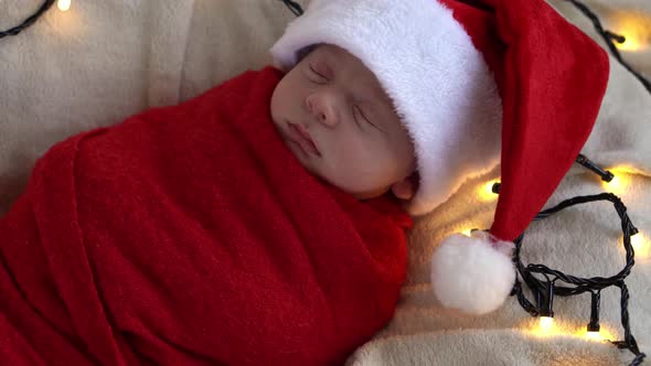 Close Up Portrait First Days Of Life Newborn Cute Funny Sleeping Baby In Santa Hat Wrapped In Red