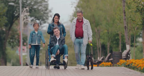 Caring Family with a Disabled Teenager Walks Through the Park on an Autumn Afternoon