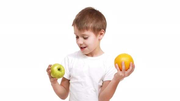 Young Smiling Caucasian Boy Holding Big Apple and Orange in Hands Exploring Them Smelling and alt