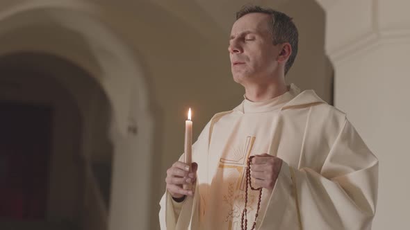 Priest in White Alb Blowing Out Candle after Pray alt