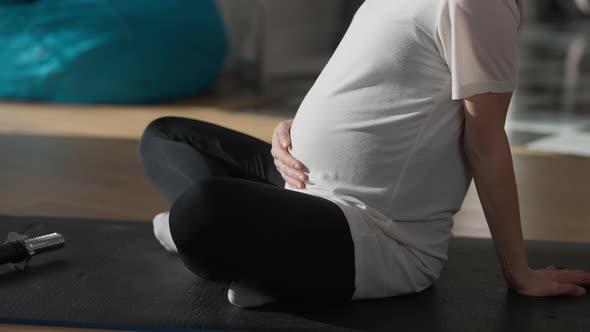 Unrecognizable Pregnant Sportswoman Caressing Belly Sitting on Exercise Mat Indoors alt