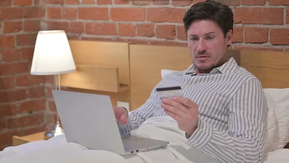 Middle Aged Man with Unsuccessful Online Payment on Laptop in Bed alt