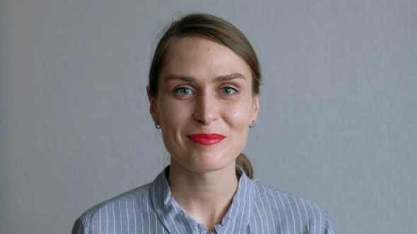 A Beautiful Girl Fools Around And Shows Her Tongue on Background of White Wall. alt