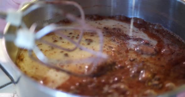 A chef pouring milk into a mixing bowl full of cocal powder and flour and using an electric mixer to alt