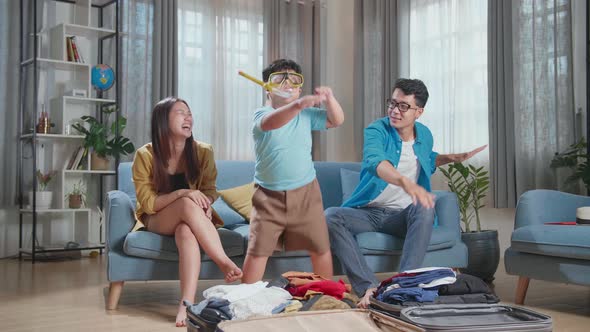 Funny Asian Family Packing Clothes In A Suitcase For A New Journey. Son Wearing Scuba Diver Mask alt