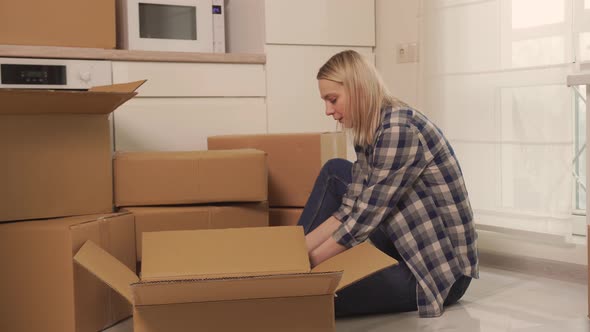 A Woman Sitting on the Floor Puts Dishes in Cardboard Boxes