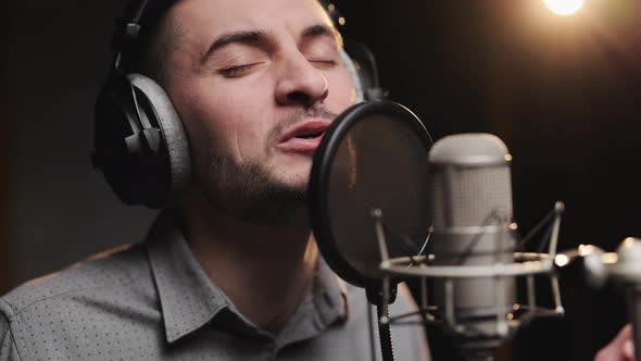 Professiona Caucasian Male Singer Wearing Headphones is Performing a New Song With Microphone