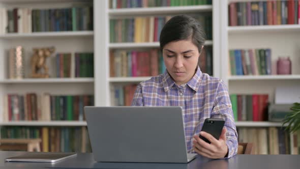 Indian Woman using Smartphone while using Laptop in Office alt